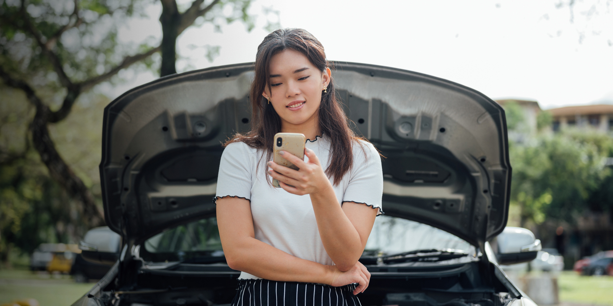 woman looking at phone with car hood up