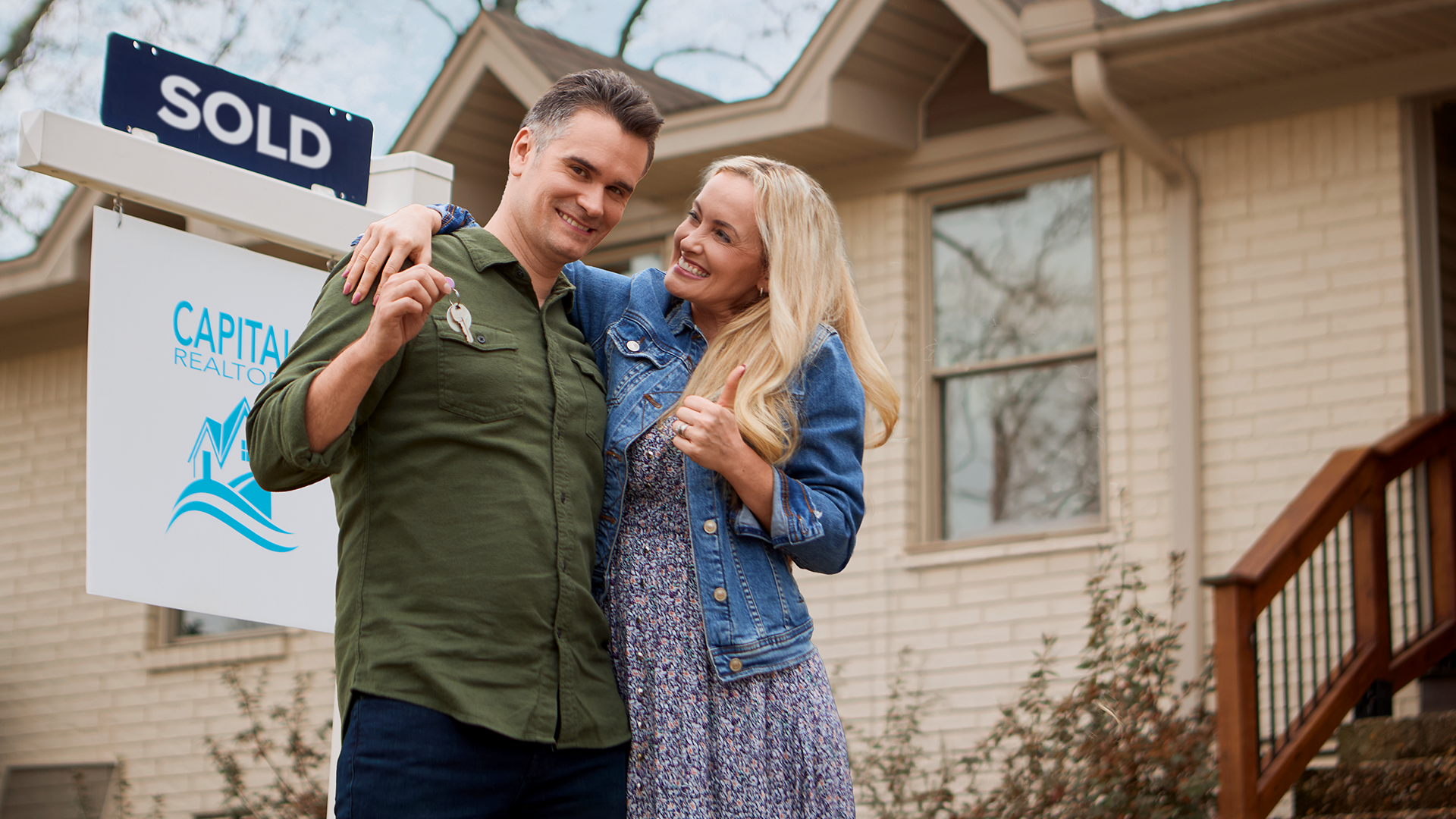 Happy couple in front house with a sold sign